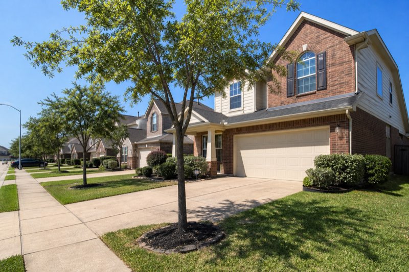 Two-story 2000s brick tract home on a sidewalk-lined master-planned community street
